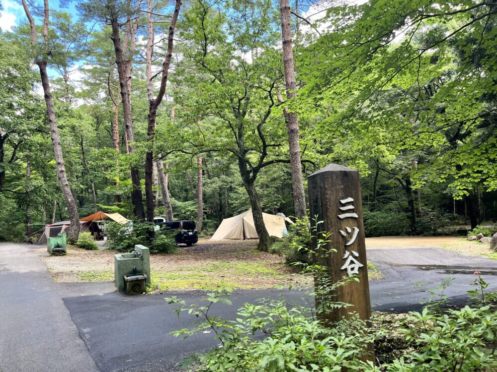 三ツ谷の案内看板と木々の間に張られたテント